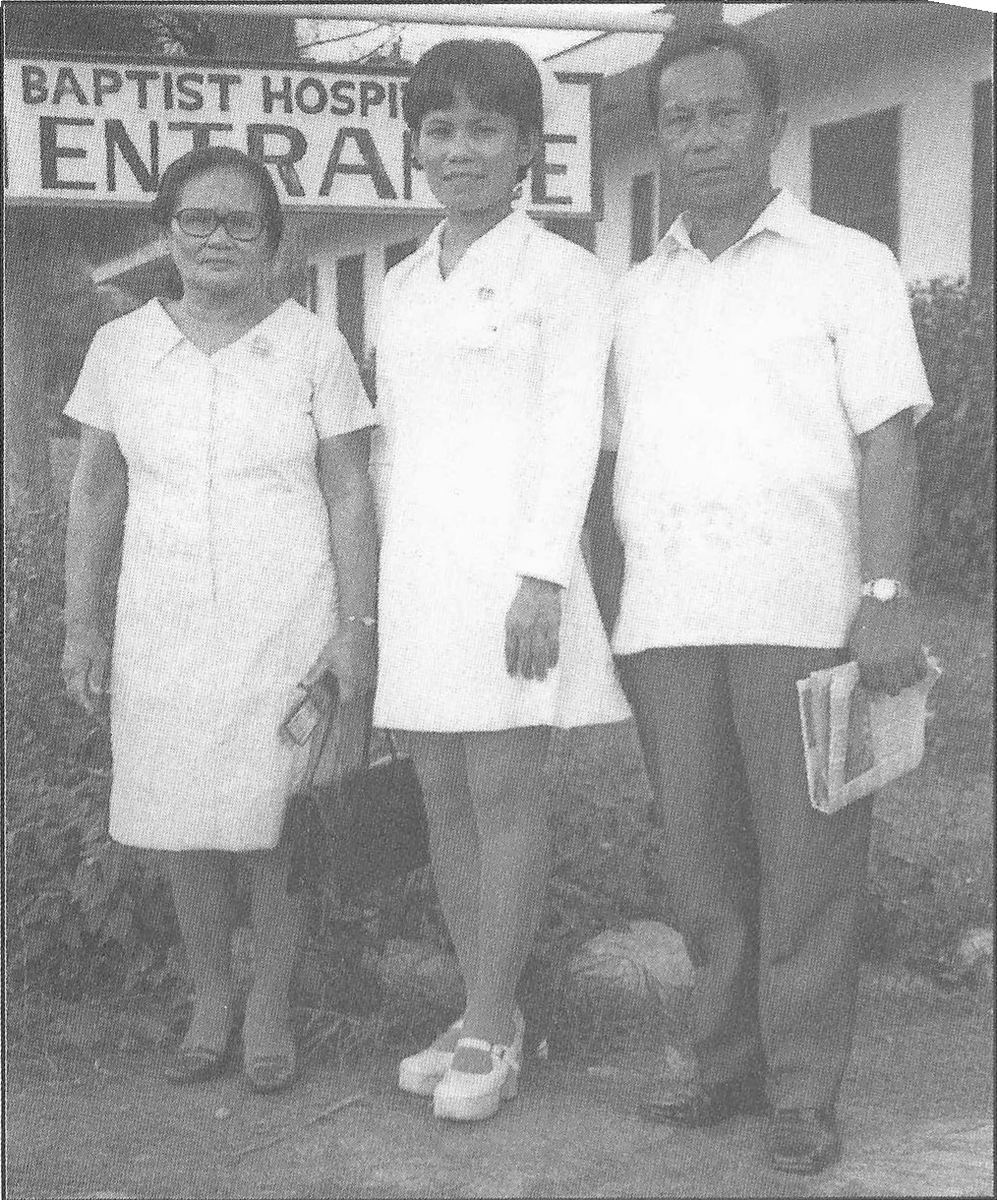 Three people standing before a sign reading Baptist Hospital Entrance.