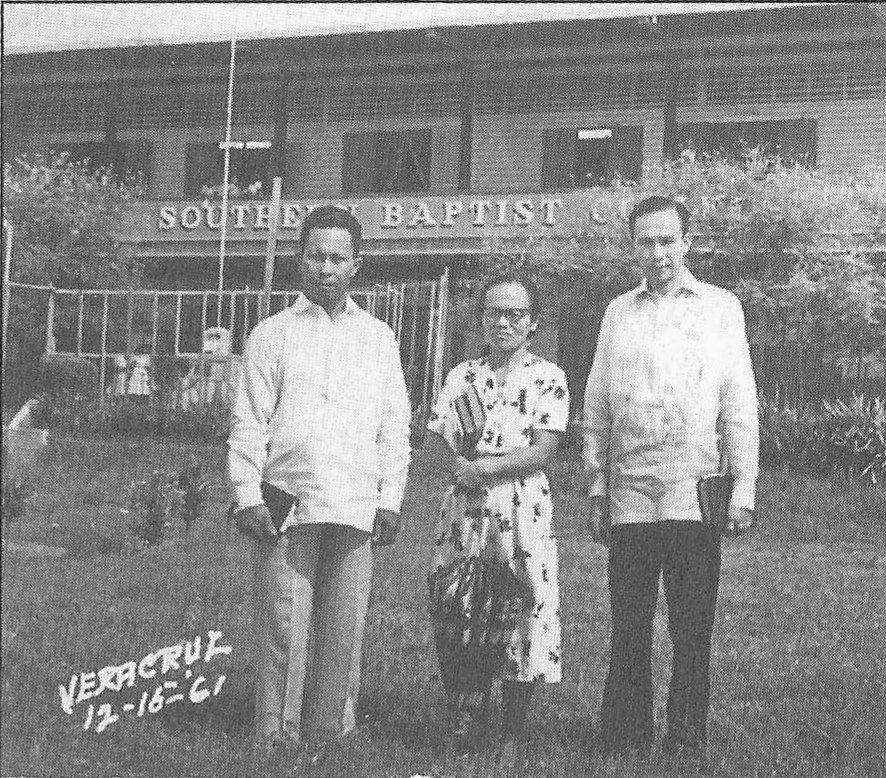 Three people standing on the lawn in front of the Southern Baptist College building.
