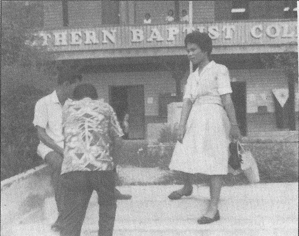 A young woman standing with classmates outside the Southern Baptist College building.